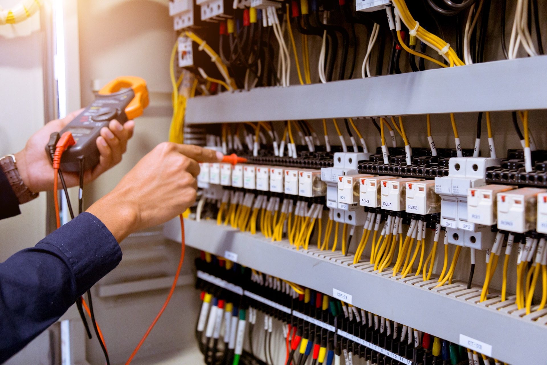 Technik meria elektrický prúd klieštovým multimetrom na otvorenom rozvádzači s farebnou kabelážou